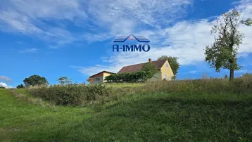 Ländliches Haus auf einem Hügel mit weitem Blick über die grüne Landschaft unter blauem Himmel.