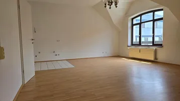 Helles Zimmer im Dachgeschoss mit Holzboden, großem Fenster und schräger Decke, bereit zur Gestaltung.