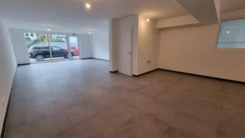 Geräumiger, leerer Gewerberaum mit großen Fenstern und modernen Fliesenböden, ideal für Büro oder Laden.