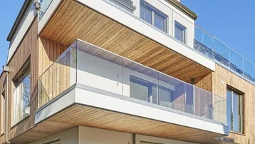 Moderne Architektur mit mehreren Balkonen und Holzverkleidung unter blauem Himmel.