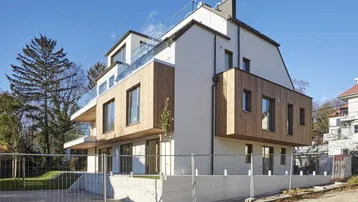Modernes Mehrfamilienhaus mit weißer Fassade, Holzverkleidung und Glasbalkonen in sonniger Umgebung.