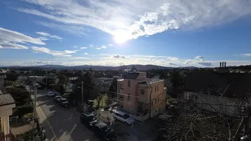 Weitläufiger Blick über eine Wohngegend mit Bergen im Hintergrund unter blauem Himmel und Sonnenschein.