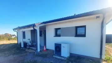 Seitenansicht des Neubaus mit Wärmepumpe, dunklen Fenstern und klarem blauen Himmel.