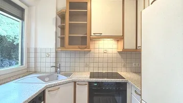 Helle Küche mit Einbauschränken, Spüle am Fenster und integriertem Kochfeld.