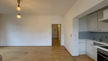 Heller Wohnbereich mit Holzboden und integrierter Küchenzeile, ideal für offenes Wohnen.
