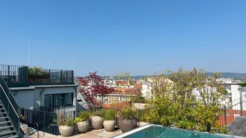 Dachterrasse mit Infinity-Pool und weitem Blick über die Stadt an einem sonnigen Tag.