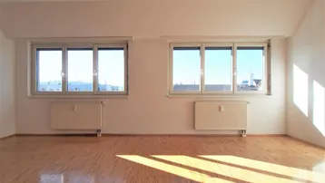 Helles, leeres Zimmer mit Parkettboden und zwei großen Fenstern, durch die Sonnenlicht einfällt.