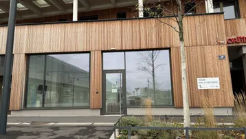 Moderne Geschäftsfassade im Erdgeschoss mit großen Glasflächen und Holzverkleidung, ideal für Büro oder Fitnesscenter.