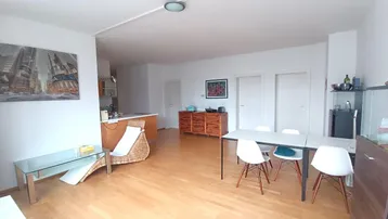 Helles, offenes Wohn-Esszimmer mit Holzboden und integrierter Küche im Hintergrund.