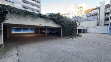Außenparkplatz mit überdachtem Bereich und Zufahrt zu Garagen, umgeben von Wohngebäuden.