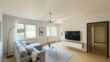 Helles Wohnzimmer mit modernem Sofa, Holzboden und Blick ins Grüne durch große Fenster.