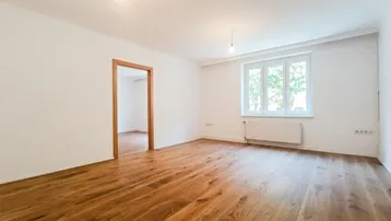 Helles, leeres Zimmer mit neuem Holzboden und weiß gestrichenen Wänden, bereit zur Einrichtung.