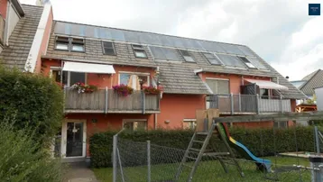 Mehrfamilienhaus mit Photovoltaikanlage auf dem Dach, Balkonen und einem Spielplatz im Gartenbereich.