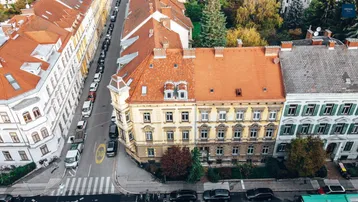 Luftaufnahme eines historischen Wohngebäudes mit rotem Ziegeldach und umliegenden Straßen.