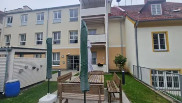 Außenansicht des Gebäudes mit einem kleinen Gartenbereich und Sitzgelegenheiten im Freien.