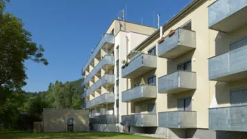 Modernes Mehrfamilienhaus mit Balkonen und gepflegter Grünfläche unter blauem Himmel.