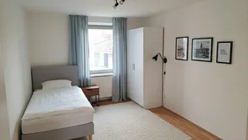 Gemütliches Schlafzimmer mit Einzelbett, Teppich und Parkettboden, hell und modern eingerichtet.
