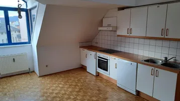 Kleine Einbauküche im Dachgeschoss mit Herd, Spüle und weißen Schränken unter der Dachschräge.