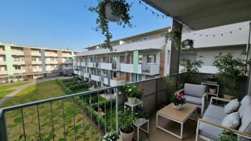 Möblierter Balkon mit gemütlicher Sitzecke, Pflanzen und Blick auf die umliegenden Gebäude und Grünflächen.