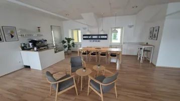 Heller und moderner Co-Working-Bereich mit Café-Theke, Esstischen und bequemen Sitzgelegenheiten.