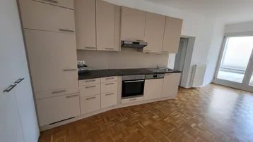 Funktionale Einbauküche mit beigen Schränken, dunkler Arbeitsplatte und Parkettboden.