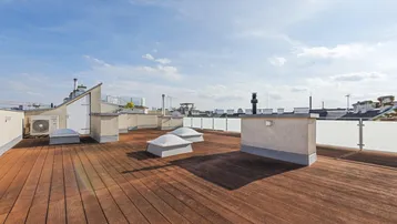 Geräumige Dachterrasse mit Holzboden, Glasgeländer und weitem Blick über die Stadt.