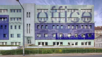 Modernes Bürogebäude mit auffälliger blau-grüner Fassade und großen Fenstern, sichtbar von der Straße.