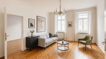 Helles Wohnzimmer mit Fischgrätparkett, Stuckdecke und klassischem Kronleuchter, möbliert.