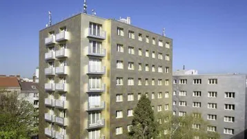 Mehrstöckiges Wohngebäude mit zahlreichen Balkonen und Fenstern unter blauem Himmel.