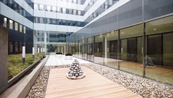 Moderner Innenhof mit Holzdeck, Kiesflächen und Glasfassaden, der eine ruhige Oase im Gebäudeensemble bildet.