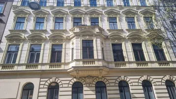 Klassische Fassade eines Altbaus mit reich verzierten Fenstern und einem Erker in hellem Beige.