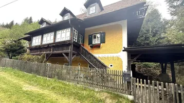 Traditionelles Haus mit gelber Fassade, Holzbalkonen und Satteldach in ländlicher Umgebung.
