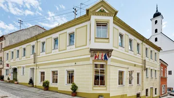 Historisches Gebäude in Gelb an einer Straßenecke mit traditioneller Architektur und Kirchturm im Hintergrund.