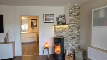 Wohnzimmer mit modernem Holzofen, Steinwandverkleidung und Zugang zur Küche.