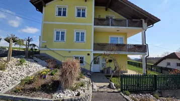 Gelbes Einfamilienhaus mit Satteldach, Balkonen und gepflegtem Vorgarten in ländlicher Umgebung.