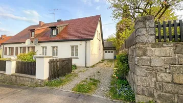 Weißes Einfamilienhaus mit rotem Ziegeldach, Kiesauffahrt und Steinmauer.