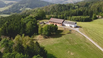 Ländliches Anwesen mit mehreren Gebäuden, umgeben von Wäldern und Feldern in hügeliger Landschaft.