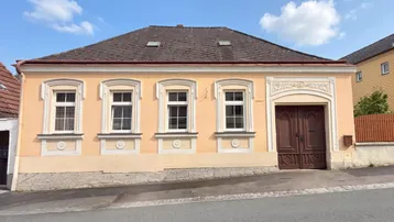 Vorderansicht eines charmanten Hauses mit traditioneller Architektur und hellgelber Fassade unter blauem Himmel.