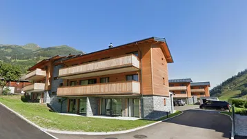 Modernes Mehrfamilienhaus in Holz- und Steinkonstruktion mit Balkonen und Bergblick in alpiner Umgebung.