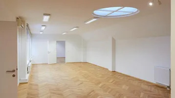 Geräumiger Büroraum mit Fischgrätparkett, Oberlicht und großen Fenstern für viel Tageslicht.