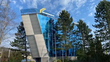 Modernes Bürogebäude mit blauer Glasfassade und markanter Architektur unter blauem Himmel.