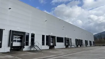 Großes Industriegebäude mit zahlreichen Laderampen und einer weiten Zufahrtsfläche unter bewölktem Himmel.