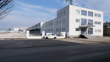 Weißes Geschäftsgebäude mit blauen Akzenten und einem großen Parkplatz davor unter blauem Himmel.
