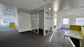 Geräumiges Büro mit Teppichboden, Glasabtrennungen und Arbeitsplätzen mit gelben Trennwänden.
