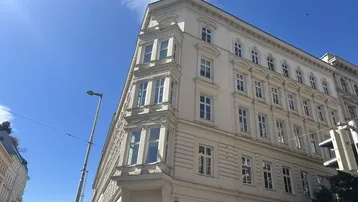 Klassisches Eckgebäude mit vielen Fenstern und historischer Architektur unter blauem Himmel.