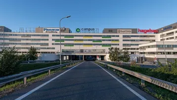 Moderne Bürogebäude mit farbigen Akzenten und Zufahrtsstraße unter blauem Himmel.