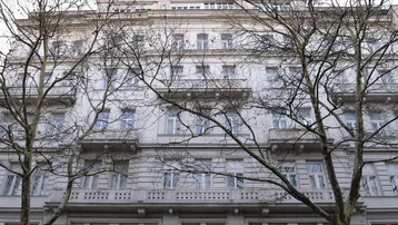 Klassisches Mehrfamilienhaus mit eleganter Fassade, vielen Fenstern und Balkonen, umgeben von kahlen Bäumen.