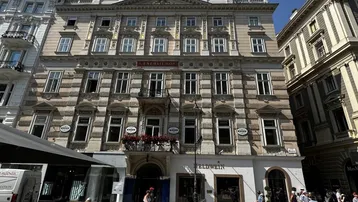 Historisches Gebäude mit aufwendiger Fassade und Geschäften im Erdgeschoss an einer belebten Straße.