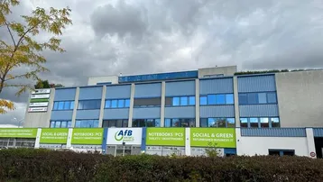Außenansicht eines modernen Geschäftsgebäudes mit blauer Fassade und grünen Werbeschildern unter bewölktem Himmel.