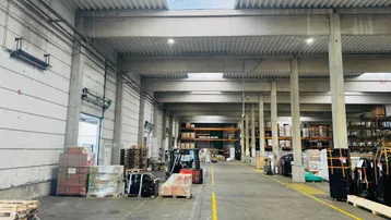 Geräumige Lagerhalle mit hohen Decken, Betonstützen und natürlichem Lichteinfall durch Oberlichter.